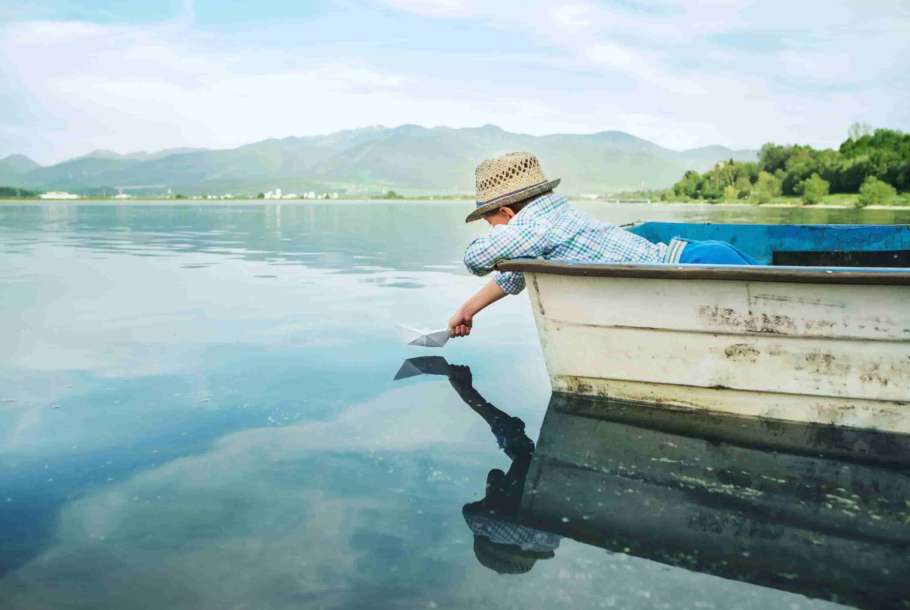 garçon posant un bateau en papier sur un lac